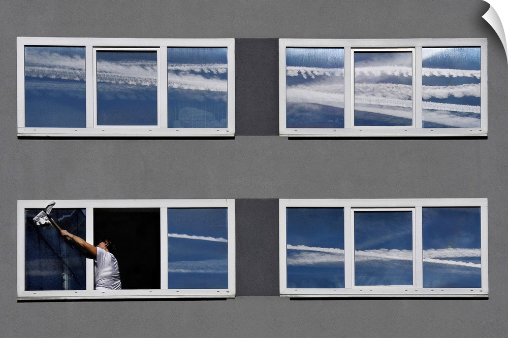 A conceptual photograph of a woman cleaning her windows of reflected vapor cloud streaks from airplanes.