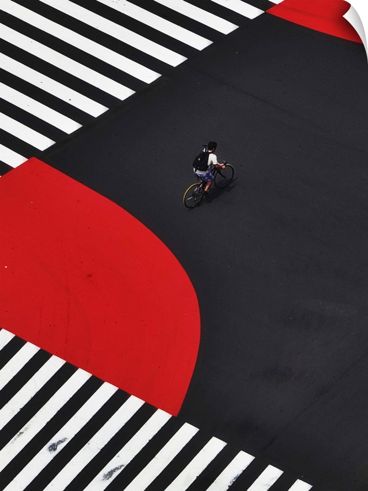 A cyclist crossing the center of a street painted with zebra crossings and red lanes.