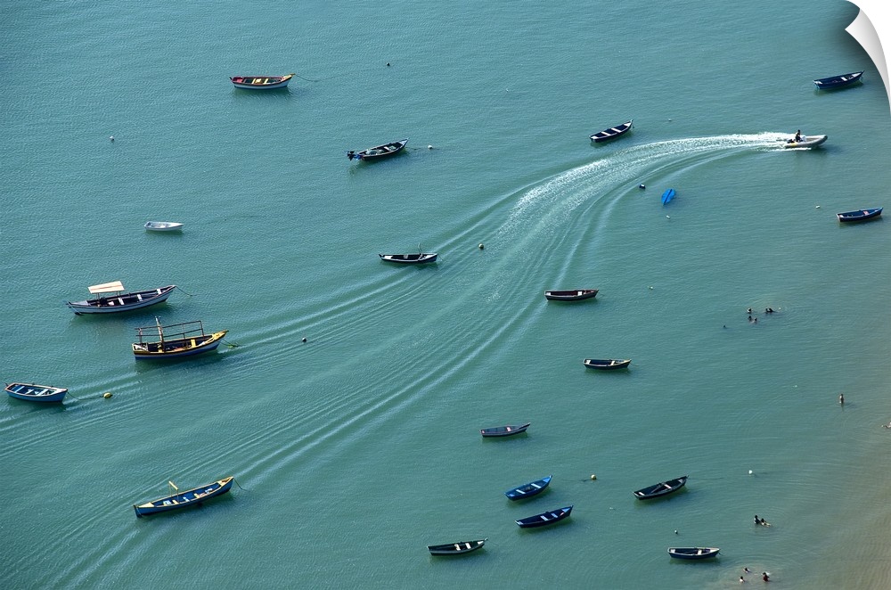 Aerial photograph of boats anchored on a teal ocean with wave lines creating movement from one motorboat in action.