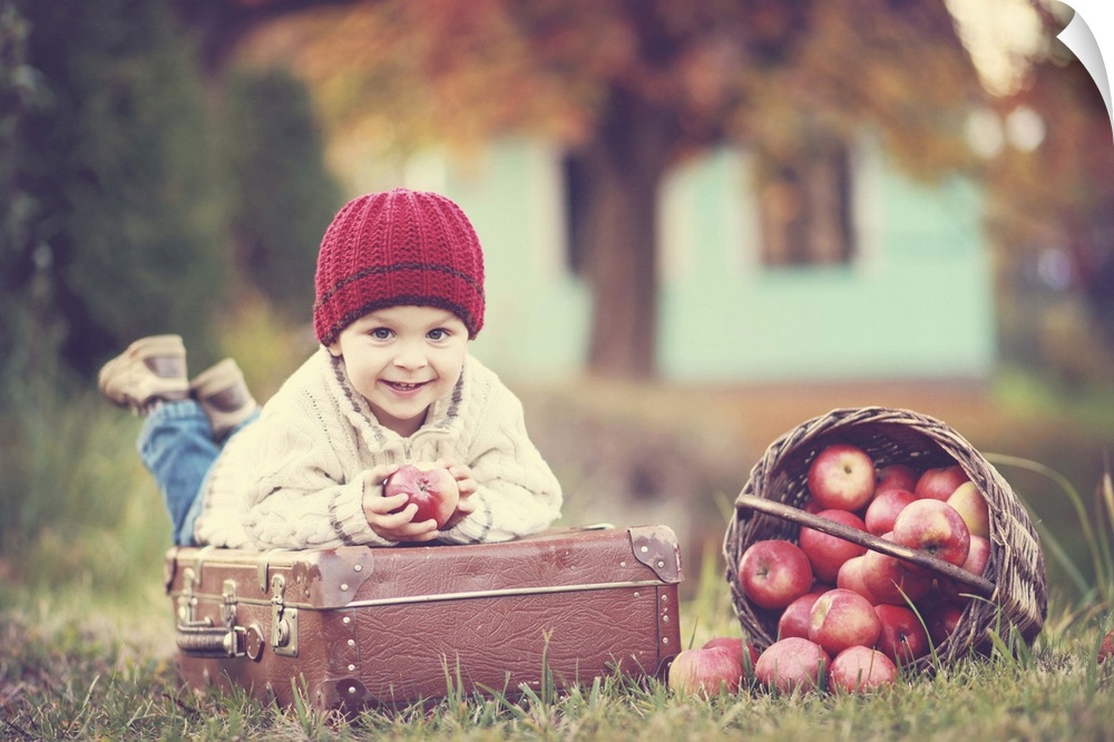 A young child holding an apple while laying on a suitcase.