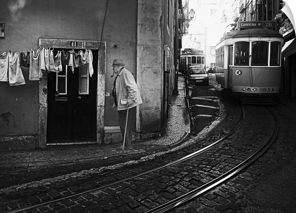 A man with a cane walking in the street of Lisbon, Portugal, with a tram passing nearby.