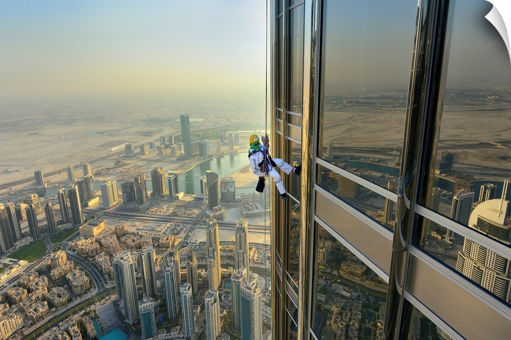 A man hooked to a harness belaying from the top of a skyscraper with a view of the city below him.