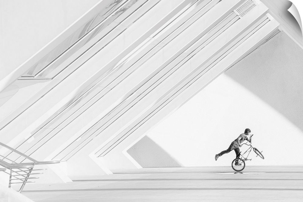 A black and white photograph of a guy riding a BMX bike under a geometric architectural structure.