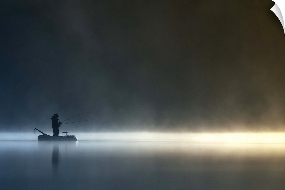 A fisherman stands in his boat on a calm, misty lake, Poland.