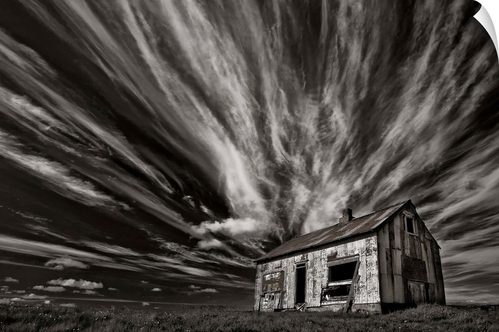 High contrast photo of a cabin in Iceland with clouds streaking overhead.