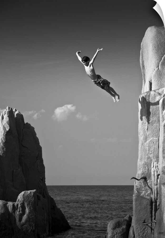 A young man leaping off a cliff into the ocean, Sardinia, Italy.