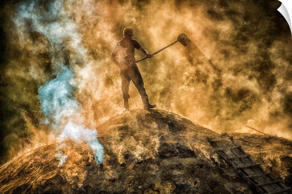 A man standing on a hilltop with a shovel obscured by smoke and fog.
