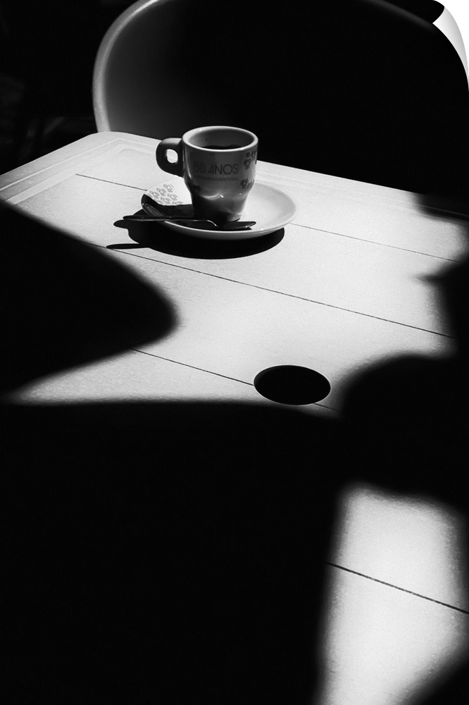 A small coffee cup and saucer sitting on an empty table covered in dark shadows.