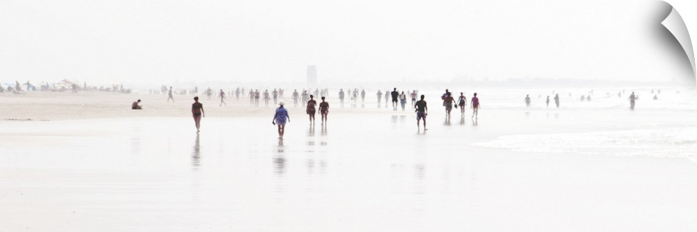 Panoramic landscape photograph of a crowd of people walking on a white, blown out beach shore with a shallow depth of fiel...