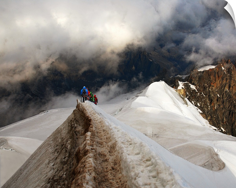 Mountain climbers trekking across a snowy peak on their way to mountains obscured by clouds.