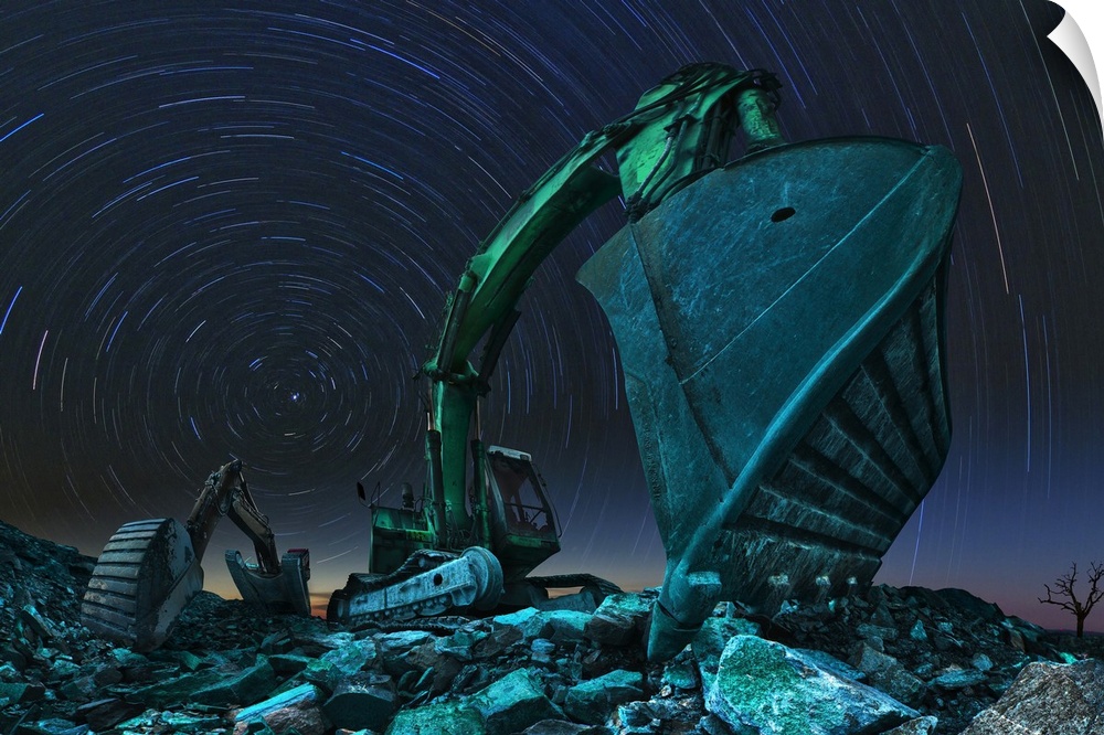 Wide angle photo of two excavators under the night sky with star trails.