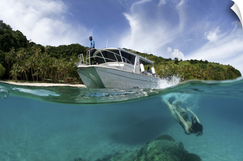 A snorkeler dives underwater near a boat in a tropical Fiji bay.