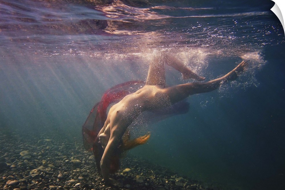 A nude woman dives in the water with a red veil, illuminated by beams of light shining through the surface.