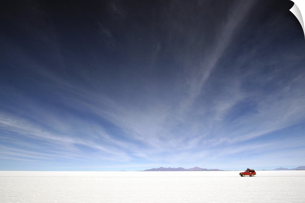 A red car traverses the Salar de Uyuni in Bolivia, a gigantic salt flat.