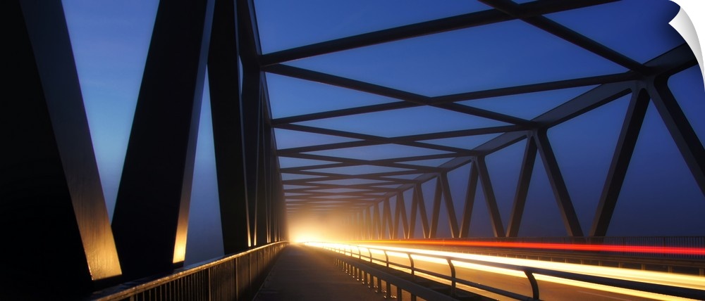 Light trails on a bridge with cross beams forming simple shapes in the morning.