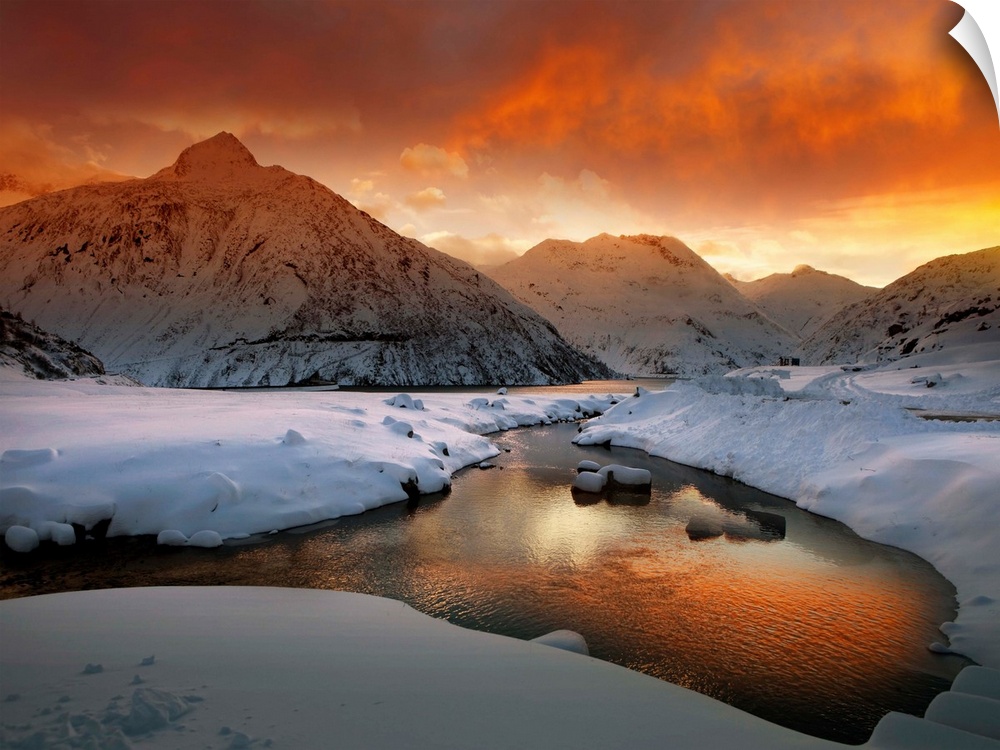 A river in a snowscape reflecting the orange color of the sunrise, in the Austrian Alps.