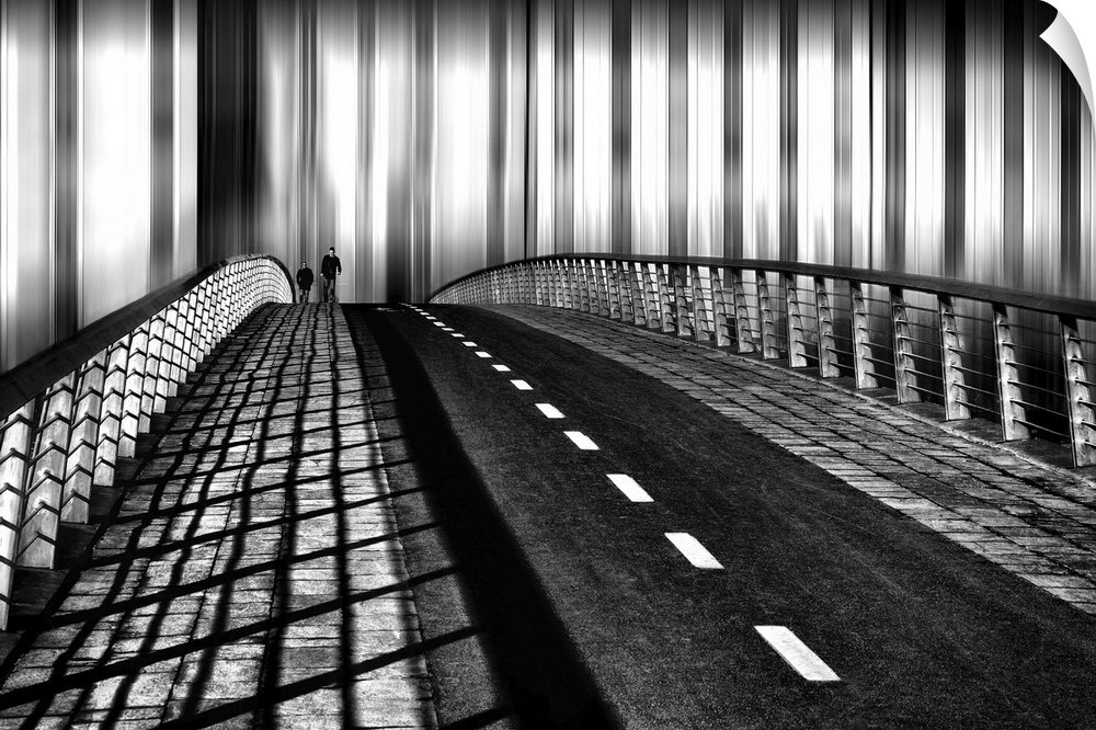 Black and white image of two people walking on the sidewalk of a bridge, with complex shadows created by the railing.
