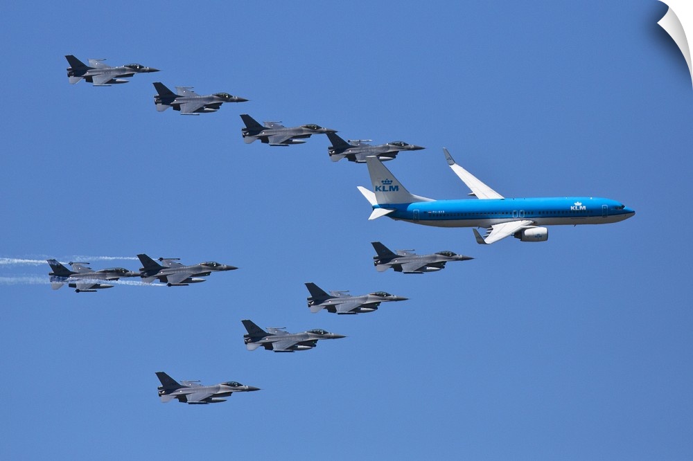 A fleet of grey jets fly in formation around a blue commercial airliner.