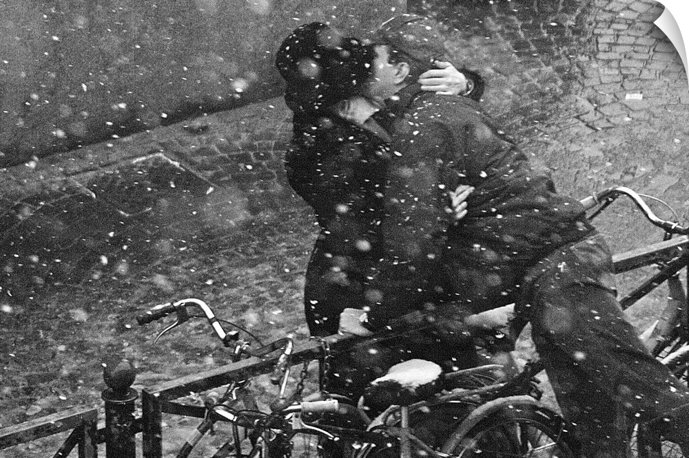 A couple in love kiss over a railing during a snowfall.