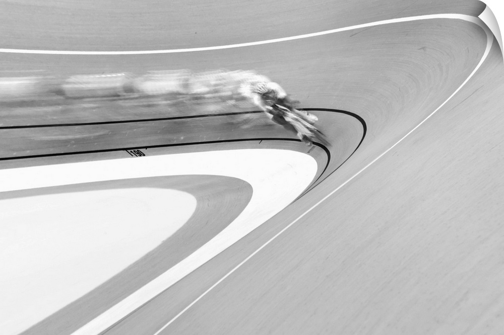 Black and white image of a cyclist in a velodrome coming around a curve.