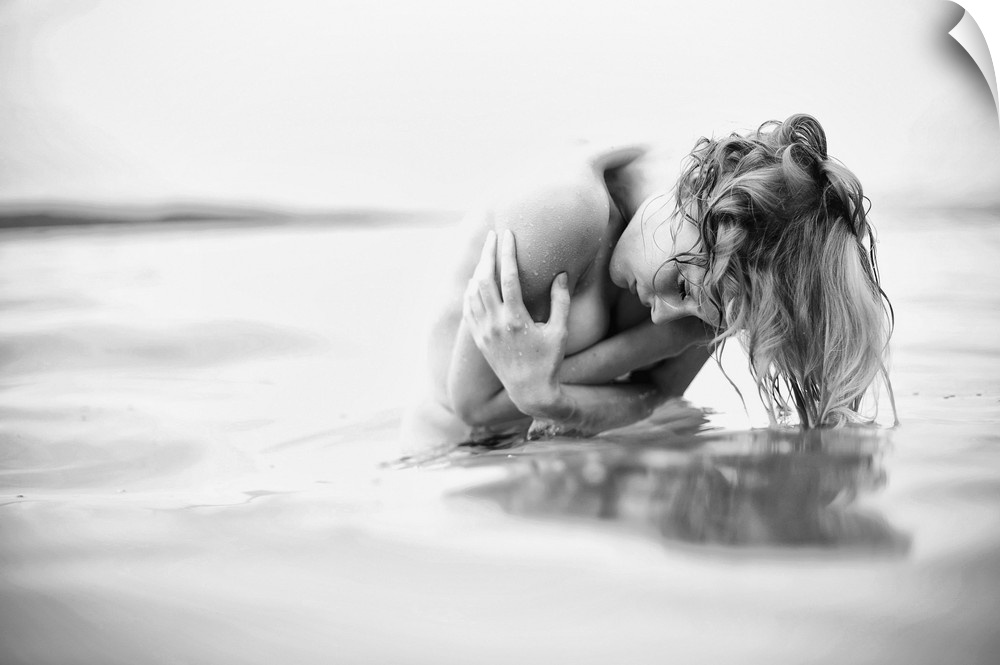 Black and white fine art portrait of a nude woman in freezing water, holding herself.