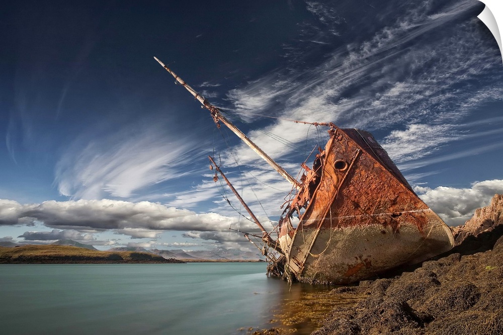 A abandoned ship sits on the shoreline, covered in rust, Stykkisholmur, Iceland.