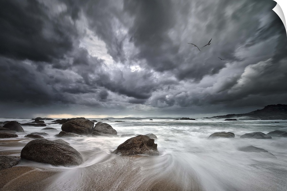 Dramatic clouds hang over a rocky beach with the tide rushing out to sea.
