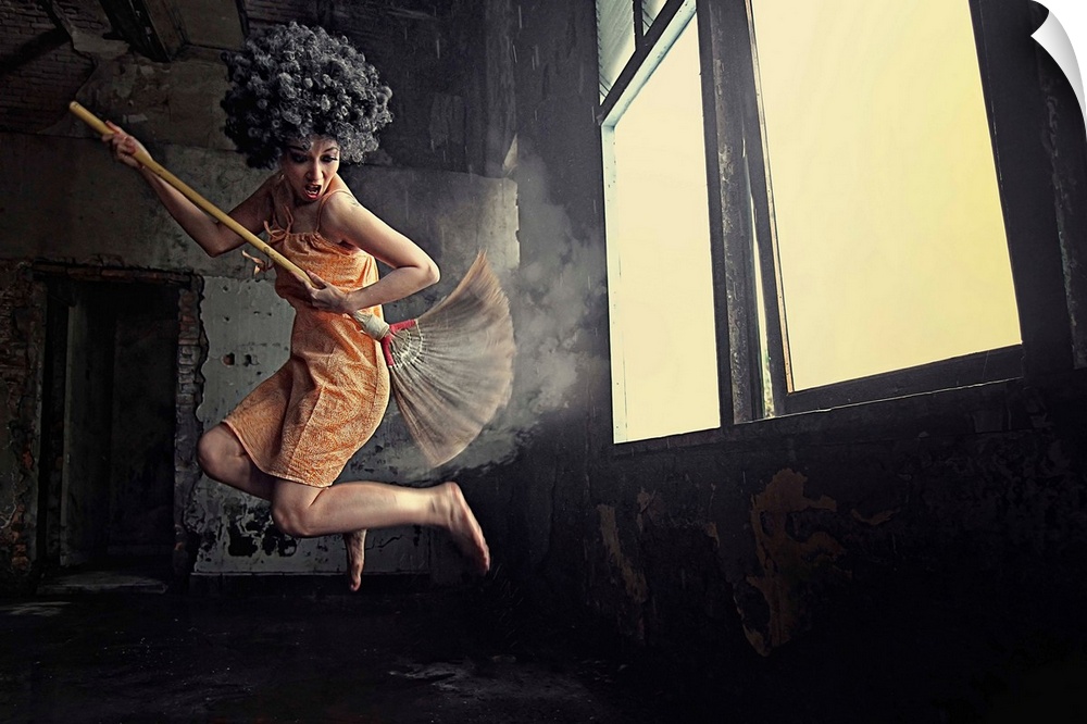 A women leaping into the air playing air guitar on a mop in front of a window.