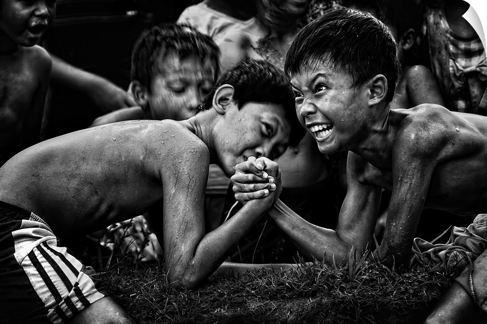 A black and white photograph of children arm wrestling with other gathered around them.