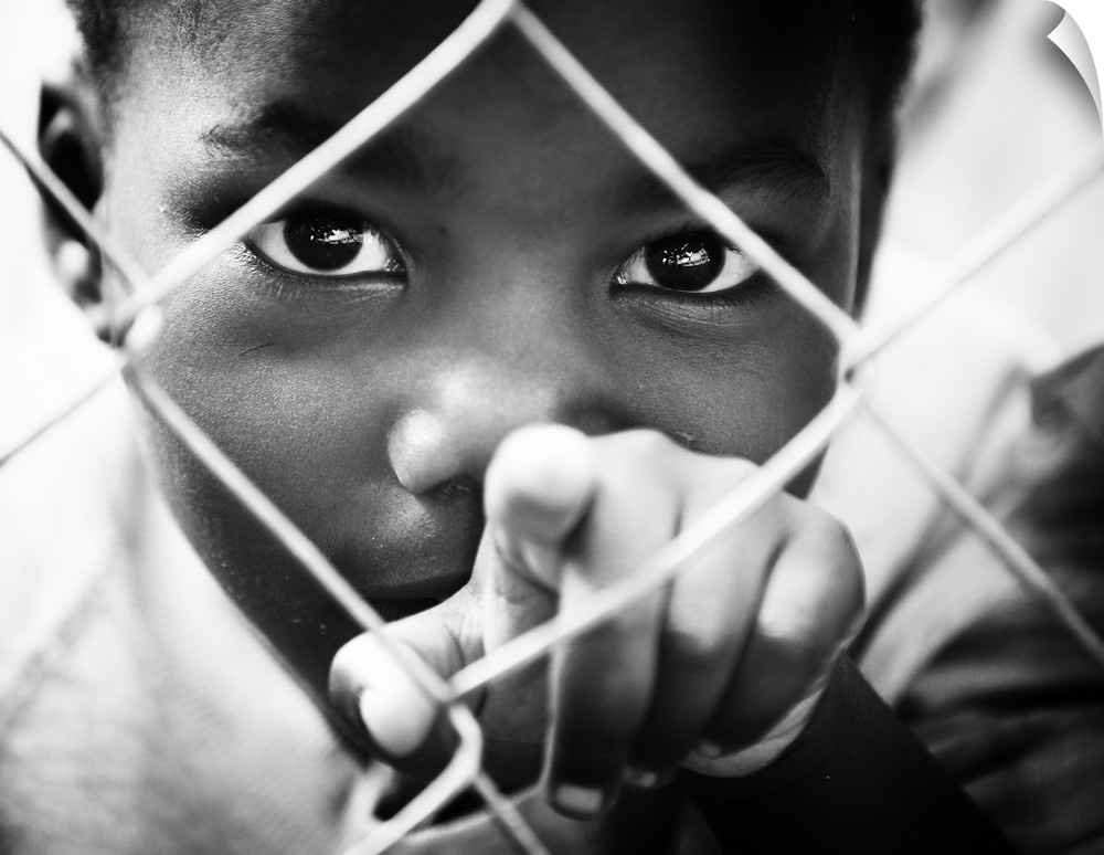 A small boy points through a chain-link fence.