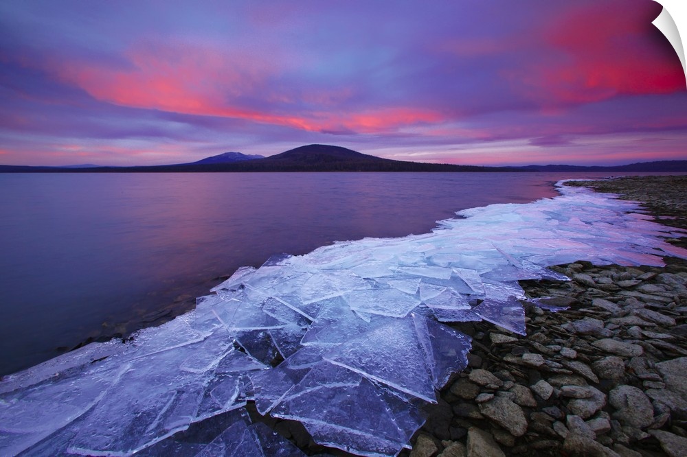 Cracked ice sheets on a rocky shore at sunrise.
