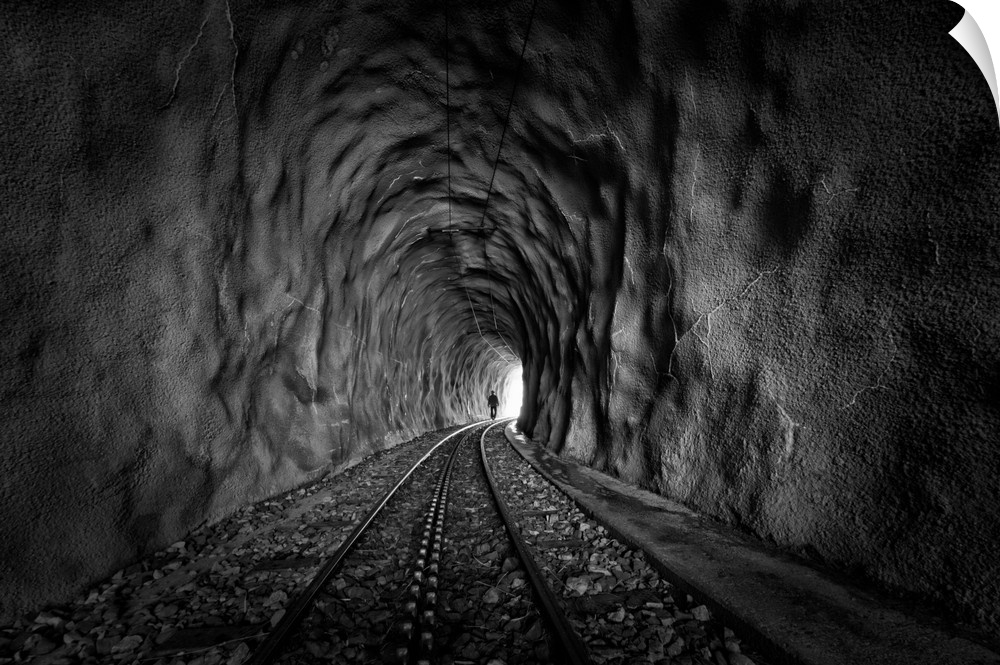 A figure walks along tracks toward the end of a tunnel.