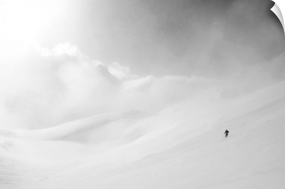 White mountain landscape of snow and clouds with a lone skier made miniature by the vast expanse.