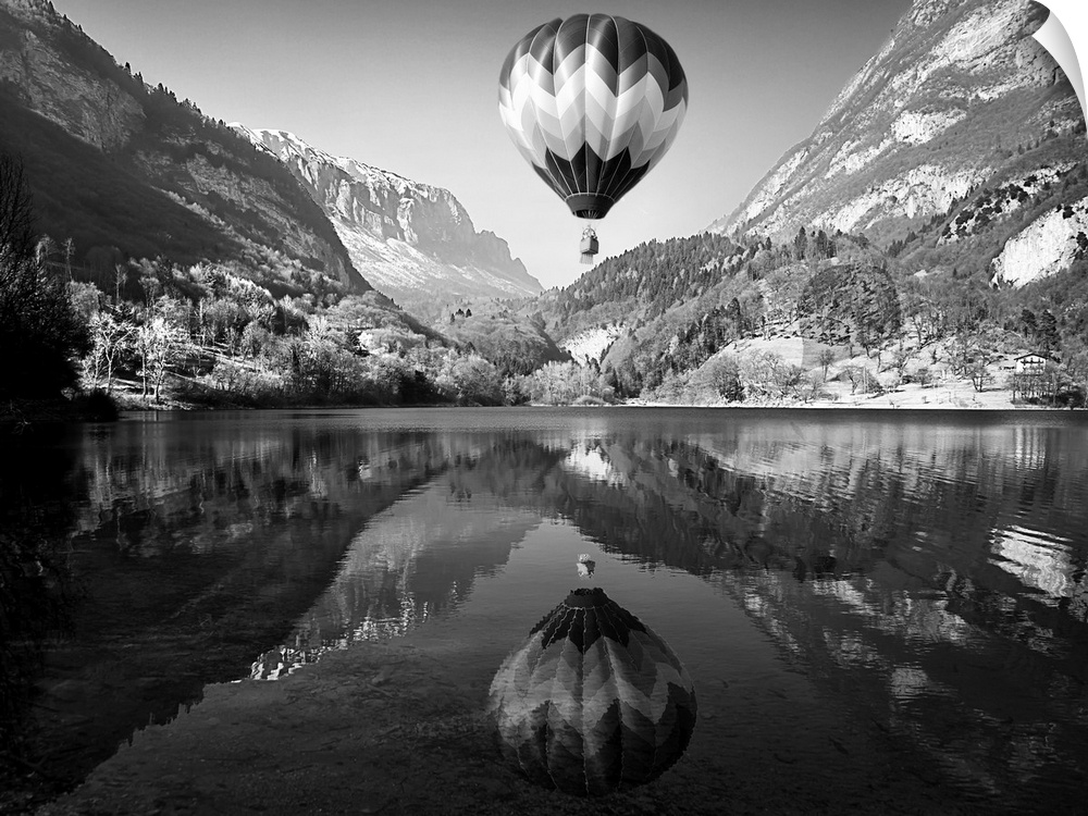Hot air balloon rising above a lake in the mountains, with its mirror reflection below.