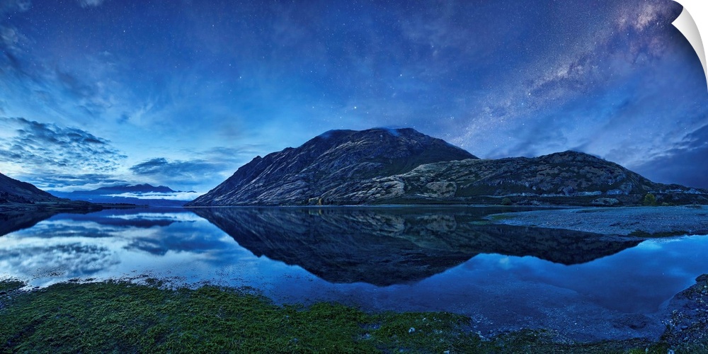 A crystal blue lake reflects its mountainous environment under starry night sky, New Zealand.
