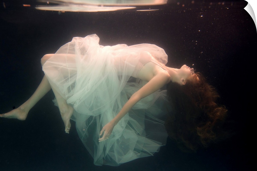 A conceptual photograph of a woman in white dress suspended under water.