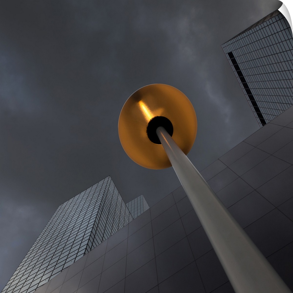View from below of a lamp near a skyscraper, with dark clouds above.
