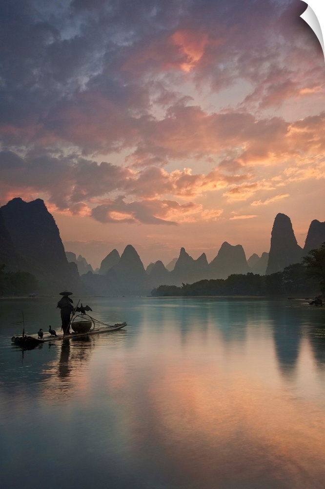 A fisherman on a boat in the Li River, with beautifully colored clouds at sunrise, China.