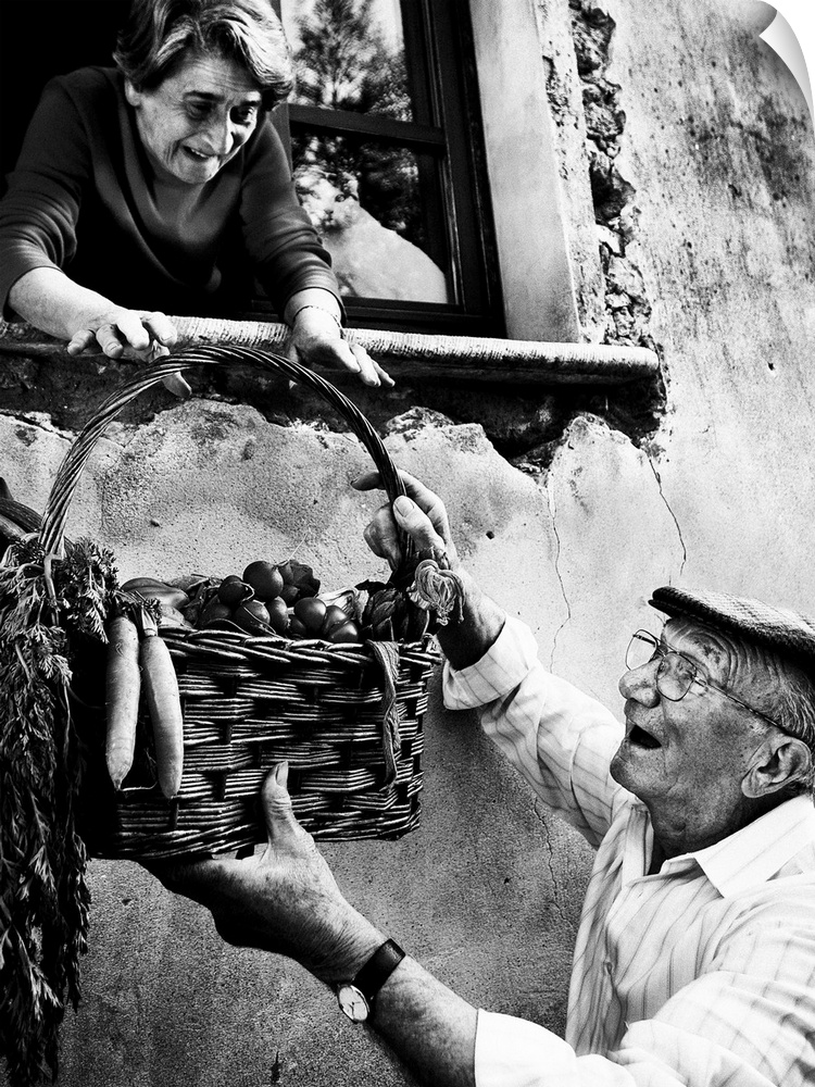 A man handing a basket of fresh vegetables to a woman in a window.
