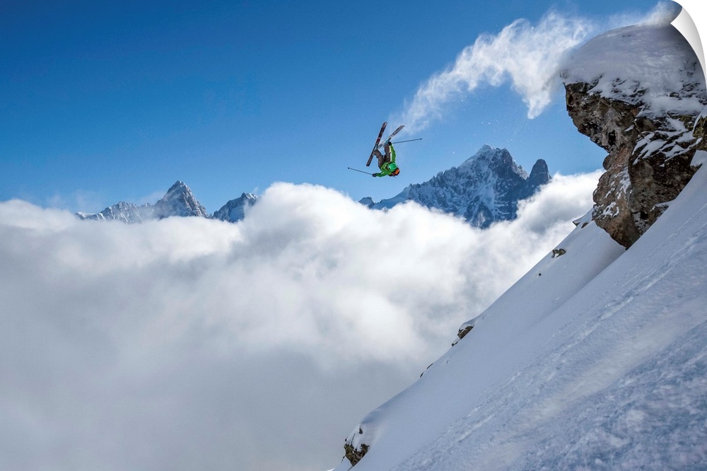 A skier leaps off a mountain in France, kicking off snow from the ends of the skies.