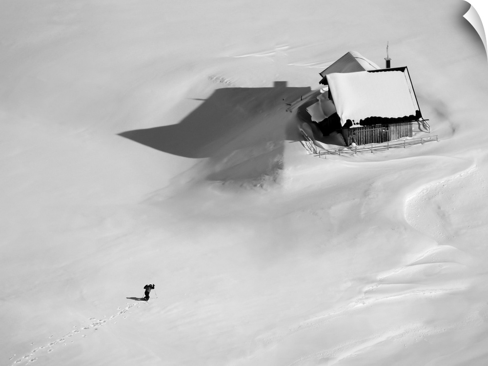 Aerial view of a skier making his way back to his house in the middle of an empty landscape with thick snow.