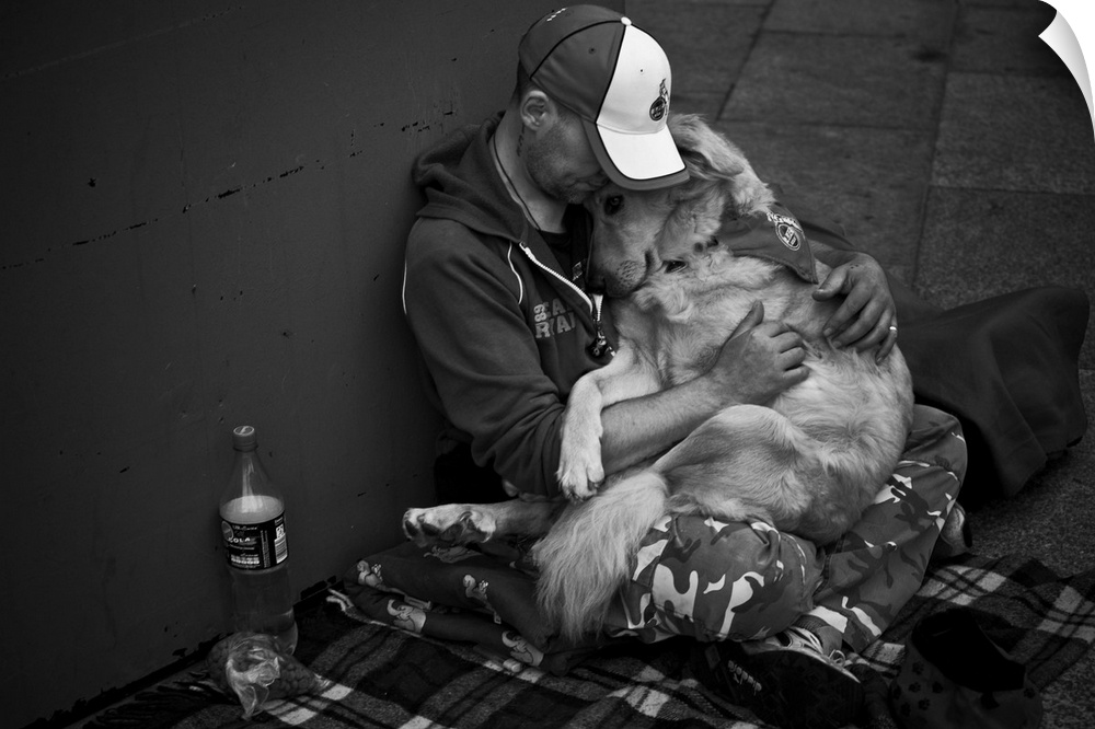 A man sitting in the street holds his dog close.