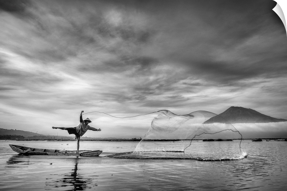A man on a canoe strikes a pose as he skillfully throws a net into the water.