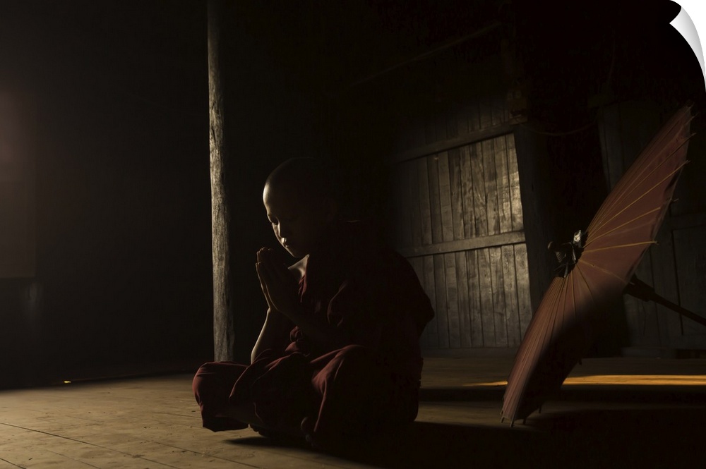 A monk praying in a  dark room with a parasol nearby.