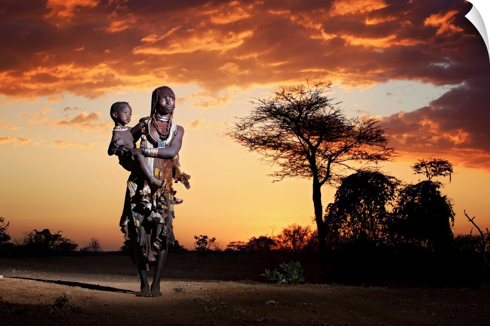 A portrait of a tribes-woman holding her child underneath a sunset sky.