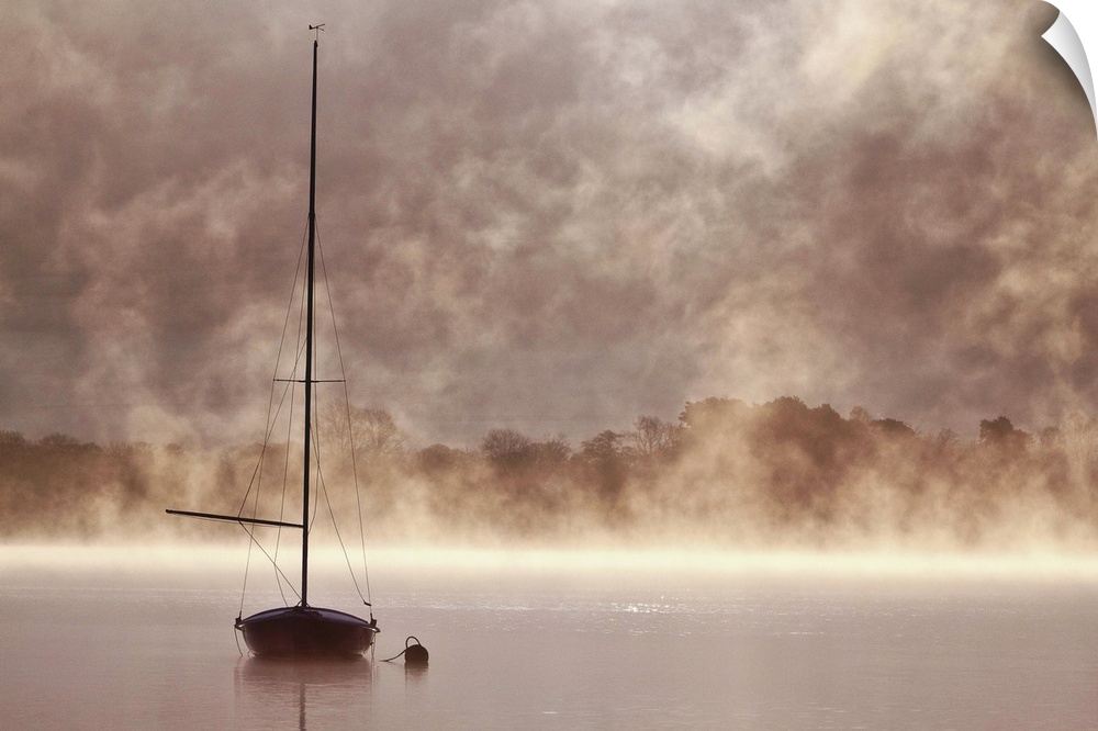 A boat with a tall mast in a misty lake in Cumbria.