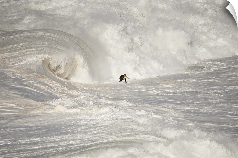 A man on a surfboard riding rough looking white waves in vast ocean.