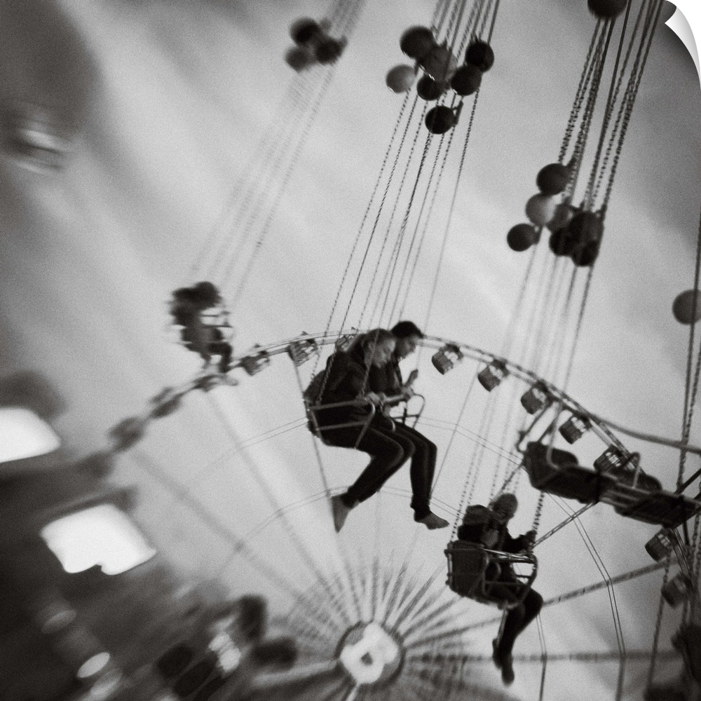 People swinging on an amusement park ride with a ferris wheel behind, Tivoli, Denmark.