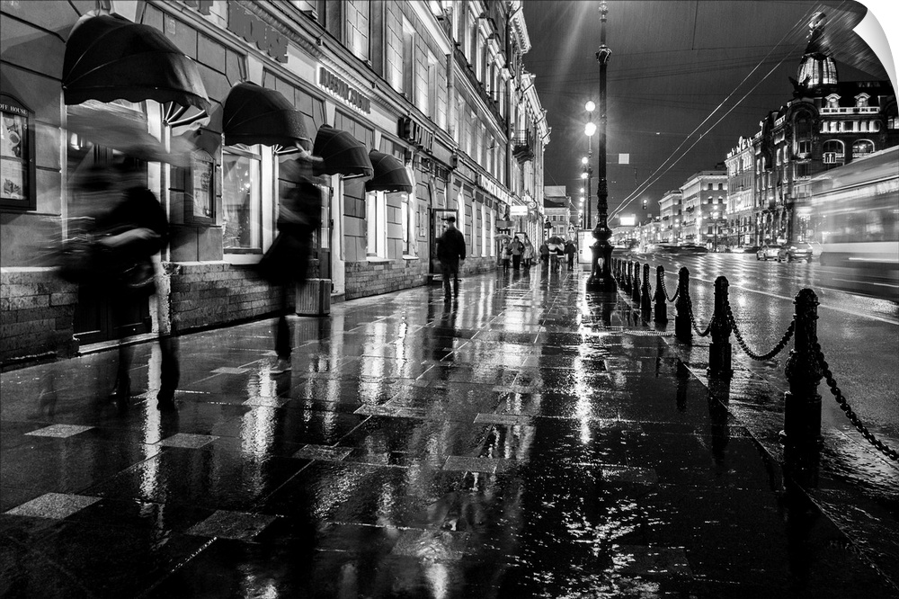 People walking on a sidewalk in the city at night, trying to get out of the rain.