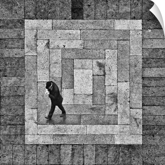 A man walking on a stone street which creates a square when viewed form above.